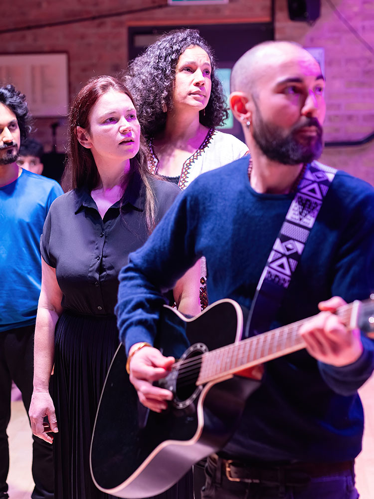 image of four people looking to the right, one man in the front playing the guitar