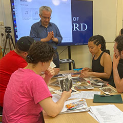 Image of a group of students seating at a table looking at materials from the archive and a teacher with an interactive screen behind him